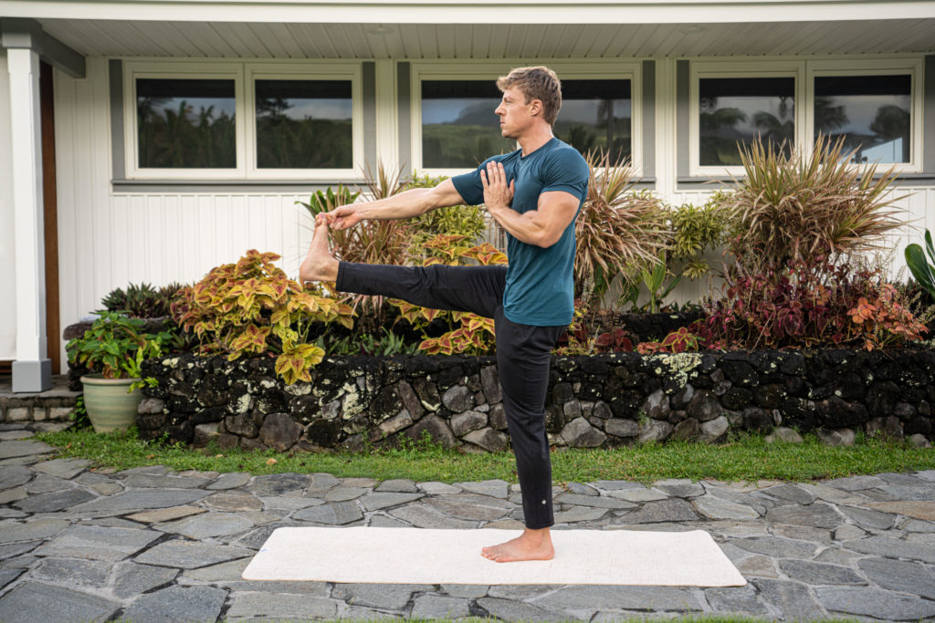 Mężczyzna wykonujący Pozycję jogi z Wyciągniętą Nogą (Utthita Hasta Padangusthasana) na jasnej macie do jogi 'Mata Home 4 mm (Decathlon)' w ogrodzie przed domem. Szkoła jogi w Rzeszowie - recenzja mat do jogi.